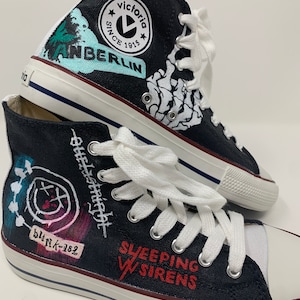 Könnte beinhalten: Schwarze High-Top-Canvas-Sneaker mit individuell bemalten Designs. Die Designs beinhalten einen Totenkopf mit Knochen, ein Band-Logo und den Text "Sleeping With Sirens".