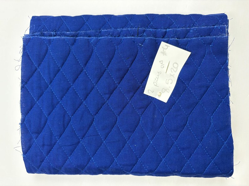 K&ouml;nnte beinhalten: Gefalteter, gesteppter blauer Stoff mit Rautenmuster. Ein kleines wei&szlig;es Etikett ist angebracht, mit dem Text "2 pcs of #4 8.5x20". Der Stoff hat einen leuchtenden Blauton.