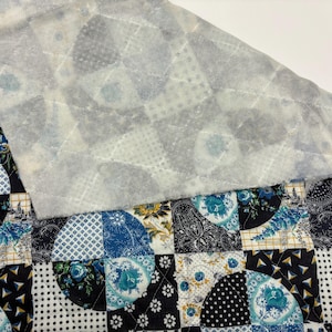 May include: A patchwork quilt featuring a mix of blue and white patterns, including floral and geometric designs. The quilt has a layer of light grey wadding on top, with a quilted pattern visible. The overall aesthetic is a blend of traditional and modern styles.