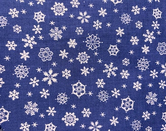 Könnte beinhalten: Nahaufnahme eines blauen Stoffes mit einem sich wiederholenden Muster aus weißen Schneeflocken. Die Schneeflocken variieren in Größe und Design und erzeugen ein winterliches oder festliches Thema. Der Stoff scheint Baumwolle oder ein ähnliches Material zu sein.