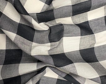 May include: Close-up of a black and white checkered fabric. The fabric has a large gingham pattern with a soft, textured appearance. The fabric is draped, showing folds and shadows, enhancing the visual depth of the material.
