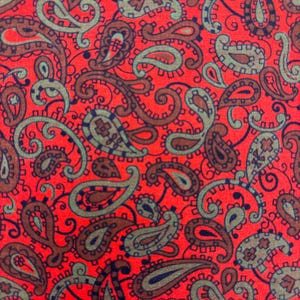 May include: Close-up of a fabric with a repeating paisley pattern. The background is a vibrant red, with the paisley designs in shades of brown, teal, and navy blue. The pattern is detailed and intricate, with curved lines and teardrop shapes.