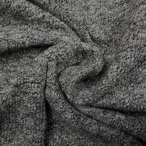 May include: Close-up of a gray and black knit fabric with a textured appearance. The fabric is draped, showing folds and shadows. The material has a speckled pattern, creating a heathered effect. This textile is suitable for clothing or home decor.