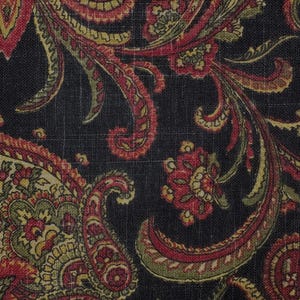 May include: Close-up of a fabric with a dark background and a detailed paisley pattern. The design features red, yellow, and green floral and scroll-like elements. The fabric has a textured appearance.