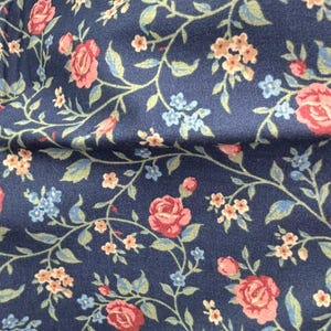 May include: A close-up of navy blue fabric with a floral design. The pattern includes red roses, small blue and peach-coloured flowers, and green leaves on twisting vines. The fabric has a soft, textured appearance.