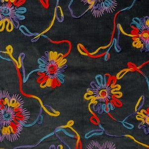 May include: Close-up of a black fabric with colorful embroidered floral patterns. The flowers are in shades of red, yellow, blue, and purple, with long, curving stems. The embroidery creates a textured, decorative design.
