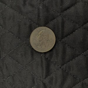 K&ouml;nnte beinhalten: Eine US-amerikanische 25-Cent-M&uuml;nze mit dem Profil von George Washington liegt auf einem schwarzen, gesteppten Stoff. Die Details der M&uuml;nze, einschlie&szlig;lich der Worte "Liberty" und "Quarter Dollar", sind sichtbar. Der Stoff hat ein Rautenmuster.