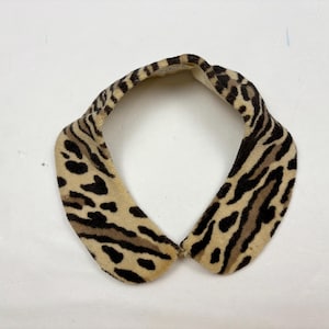 May include: A vintage collar with a faux fur animal print design. The collar features a tan base with black spots and brown stripes, creating a leopard and zebra-like pattern. The collar is curved and appears to be made of soft material.