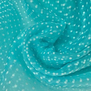 Puede incluir: Primer plano de una tela turquesa con una textura delicada y transparente. La tela está adornada con un patrón de pequeños lunares blancos, creando una estética lúdica y aireada. El material está drapeado, mostrando su calidad fluida.