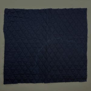 K&ouml;nnte beinhalten: Ein marineblauer, gesteppter Stoff mit einem Rautenmuster. Die Kanten des Stoffes haben einen gewellten Abschluss. Der Stoff ist einfarbig und scheint ein mittelschweres Material zu sein.