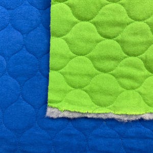May include: A quilted fabric featuring a vibrant blue section and a bright lime green section. The material has a repeating scalloped or wave-like stitched pattern across the surface, with a visible gray fuzzy lining along the bottom edge.