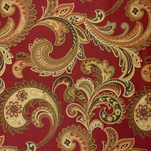 May include: Close-up of a red fabric with a detailed paisley pattern. The design features swirling, floral-inspired motifs in shades of gold, brown, and green. The fabric has a textured appearance, suggesting a woven material.