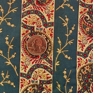 May include: Close-up of fabric with a teal background and vertical stripes. The stripes feature a paisley design in red, tan, and blue. A quarter coin rests on the fabric, providing a size reference. Delicate floral branches are also visible.