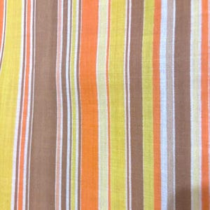 May include: Close-up of a fabric with vertical stripes in shades of yellow, orange, brown, and white. The stripes vary in width, creating a textured appearance. The fabric appears to be a woven material, possibly cotton or linen.