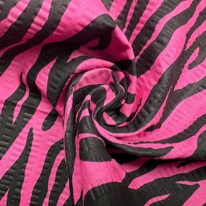 May include: Close-up of a vibrant pink fabric with a black zebra stripe pattern. The fabric is textured and appears to be folded, creating shadows and depth. The bold color combination makes a striking visual statement.