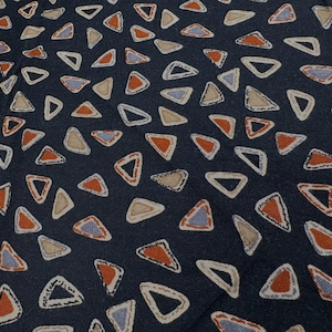 May include: Dark navy fabric with a repeating pattern of open triangles in shades of orange, tan, and blue. The triangles are outlined in white, creating a textured effect. The fabric has a subtle, woven appearance.