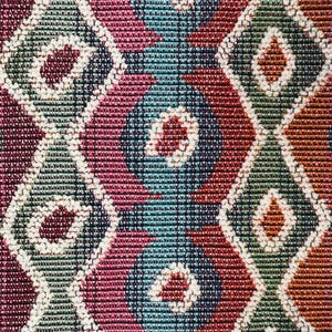 May include: Close-up of a woven fabric with a repeating geometric pattern. The design features diamond shapes in shades of blue, green, red, and orange, outlined with white. The texture appears to be tightly woven.
