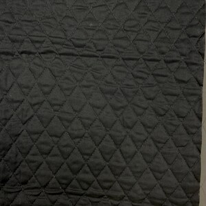 K&ouml;nnte beinhalten: Ein quadratisches St&uuml;ck schwarzes, gestepptes Gewebe mit einem Rautenmuster. Der Stoff hat eine leicht zerknitterte Textur und scheint aus einem weichen Material zu bestehen. Die Steppung erzeugt ein Raster aus Rautenformen auf der Oberfl&auml;che.