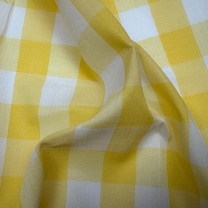May include: Close-up of yellow and white checkered fabric. The fabric is folded and draped, showing the texture and pattern of the material. The yellow squares are a bright, sunny color, and the white squares provide contrast.
