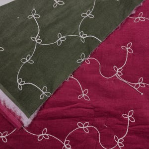 May include: Close-up of two fabric swatches. One is olive green, the other is burgundy. Both have a corduroy texture and are embroidered with a white floral vine pattern. The green swatch is layered over a white and pink material.