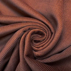 May include: A rich, dark brown fabric featuring a distinct vertical ribbed texture. The material is gathered into a central spiral, creating deep folds and shadows that highlight the consistent, linear pattern across the entire surface area.