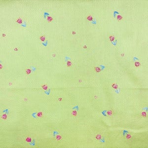 May include: A light lime green fabric featuring a repeating pattern of small pink tulips with blue stems and leaves, interspersed with tiny dark pink heart shapes. The material has a fine, textured, woven grid pattern across the entire surface.