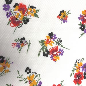 May include: White fabric with a repeating floral pattern. The flowers are in clusters and feature red, yellow, purple, and black petals with green stems. The background has a subtle textured pattern.