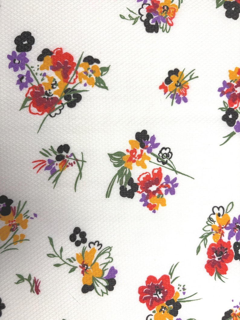 May include: White fabric with a repeating floral pattern. The flowers are in clusters and feature red, yellow, purple, and black petals with green stems. The background has a subtle textured pattern.