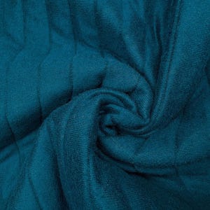 May include: Close-up of a teal fabric with a textured, ribbed pattern. The fabric is swirled, creating a spiral effect in the center. The material appears soft and pliable, with visible vertical lines.