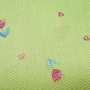 May include: A light green fabric with a textured basketweave pattern featuring small embroidered motifs. The design includes pink and blue tulips with green stems and scattered pink heart outlines stitched across the surface of the material.