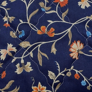 May include: A dark blue quilted fabric featuring a repeating pattern of winding vines with beige leaves and flowers in shades of orange, cream, and light blue. The material has a diamond-shaped stitched pattern across the entire surface.