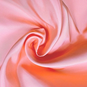 May include: A solid light pink fabric with a distinct diagonal twill weave pattern. The material is arranged in a central spiral swirl, creating soft folds and shadows that highlight the smooth, slightly reflective texture of the textile surface.