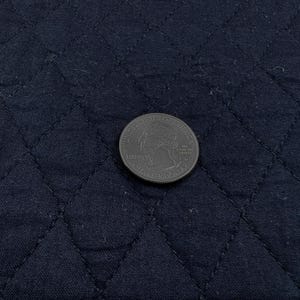 K&ouml;nnte beinhalten: Nahaufnahme eines marineblauen, gesteppten Stoffes mit Rautenmuster. Eine US-Vierteldollarm&uuml;nze liegt auf dem Stoff und dient als Gr&ouml;&szlig;enreferenz. Der Stoff hat einen dezenten Glanz.