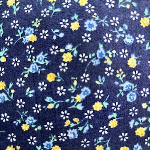 Könnte beinhalten: Nahaufnahme eines Stoffes mit dunkelblauem Hintergrund, bedeckt mit kleinen Blumenmustern. Die Blumen sind in Gelb-, Blau- und Weißtönen gehalten, mit grünen Blättern. Das Design ist ein sich wiederholendes Muster aus winzigen Blüten.