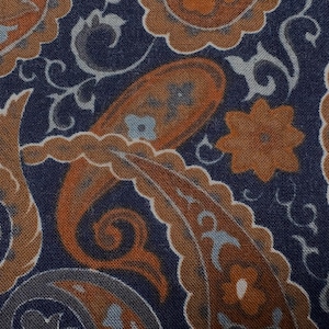 May include: Close-up of a fabric with a paisley pattern. The design features large, teardrop-shaped motifs in shades of orange and brown, set against a dark blue background. Smaller floral and scroll elements in light blue and gray complete the design.