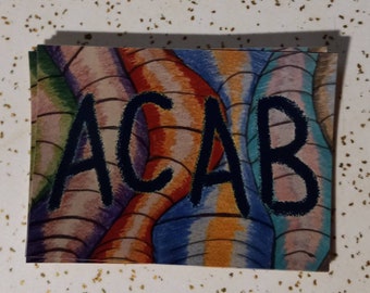 May include: A sticker with a colorful abstract background and the text "ACAB" in black outlined letters.