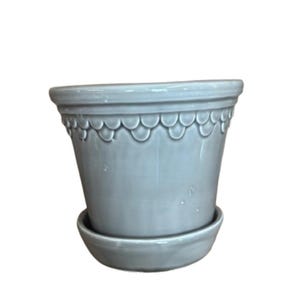 May include: A light blue ceramic flower pot with a matching saucer. The pot has a scalloped design around the top and a slightly tapered shape. The pot and saucer are made of ceramic.