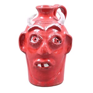 Puede incluir: Jarra de cer&aacute;mica roja con dise&ntilde;o de cara de diablo. La jarra presenta cuernos, orejas y un asa blancos. La cara tiene ojos grandes, nariz y boca con dos dientes. Un art&iacute;culo decorativo &uacute;nico.