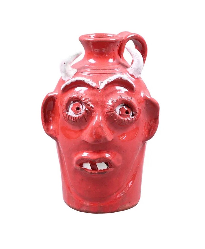 Puede incluir: Jarra de cer&aacute;mica roja con dise&ntilde;o de cara de diablo. La jarra presenta cuernos, orejas y un asa blancos. La cara tiene ojos grandes, nariz y boca con dos dientes. Un art&iacute;culo decorativo &uacute;nico.