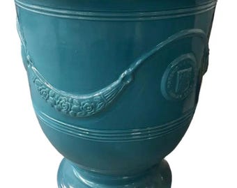 May include: A teal glazed ceramic planter with a wide rim and a pedestal base. The exterior features a relief design of a draped garland with floral details and a circular emblem with the text Poterie de la Madeleine.