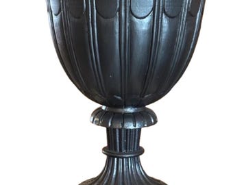 May include: A black, ornate urn with a wide, scalloped rim and a pedestal base. The urn has vertical fluting and decorative details. The base is square. This decorative piece is suitable for indoor or outdoor use.