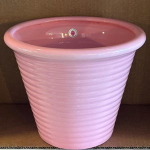 May include: A light pink, ribbed ceramic planter with a wide, rounded rim. The interior features a small, circular sticker with the text Pottery Company Los Angeles, positioned near the top edge of the basin, showcasing a glossy finish.