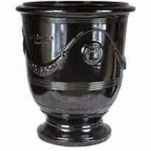 May include: A dark brown, glossy ceramic planter with a wide, flared rim and a pedestal base. The exterior features a raised, decorative relief pattern consisting of draped swags and circular medallions encircling the upper body of the vessel.