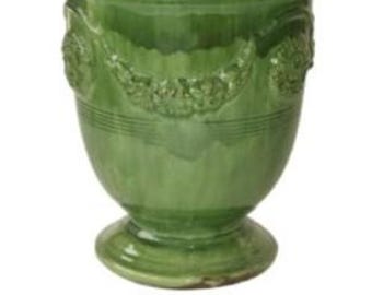 May include: A green ceramic vase with a pedestal base and a wide rim. The vase has a glossy finish and decorative relief patterns around the body. The text "VASE ANDUZE VERT" is at the bottom.