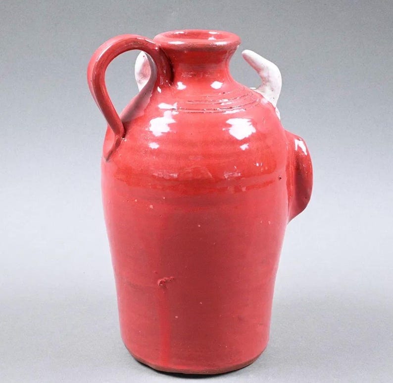 Puede incluir: Jarra de cer&aacute;mica roja con asa y dos peque&ntilde;os detalles blancos. La jarra tiene un cuerpo redondeado y un cuello estrecho. El asa es arqueada y est&aacute; unida al lateral. Probablemente utilizada para almacenar l&iacute;quidos.