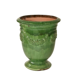 May include: A glossy, emerald green ceramic planter with a wide, flared rim and a pedestal base. The exterior features a raised relief pattern of floral garlands and circular medallions encircling the upper body, with a smooth, unglazed terracotta interior.
