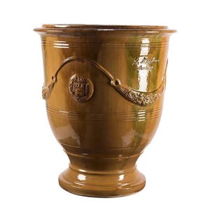 May include: A large, glazed ceramic planter in shades of brown and green. The planter features decorative relief details, including a crest and floral accents. The design includes horizontal bands and a pedestal base, suitable for outdoor or indoor use.