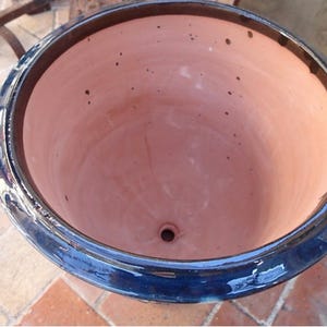 May include: A large, round ceramic planter with a glossy, deep navy blue exterior rim and a smooth, light peach-colored interior basin. The interior features a small drainage hole at the center and scattered dark brown speckles across the surface.