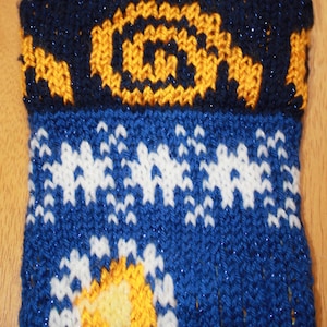 May include: A knitted blue and white oven mitt with a yellow and blue design. The top of the mitt has a navy blue pattern with a yellow design. The mitt has a loop for hanging.