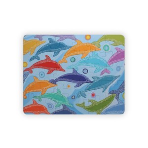 May include: A rectangular jigsaw puzzle featuring a repeating pattern of stylized dolphins in various colors including orange, blue, red, green, and purple. Each dolphin is decorated with small white dots against a light blue background with circles.